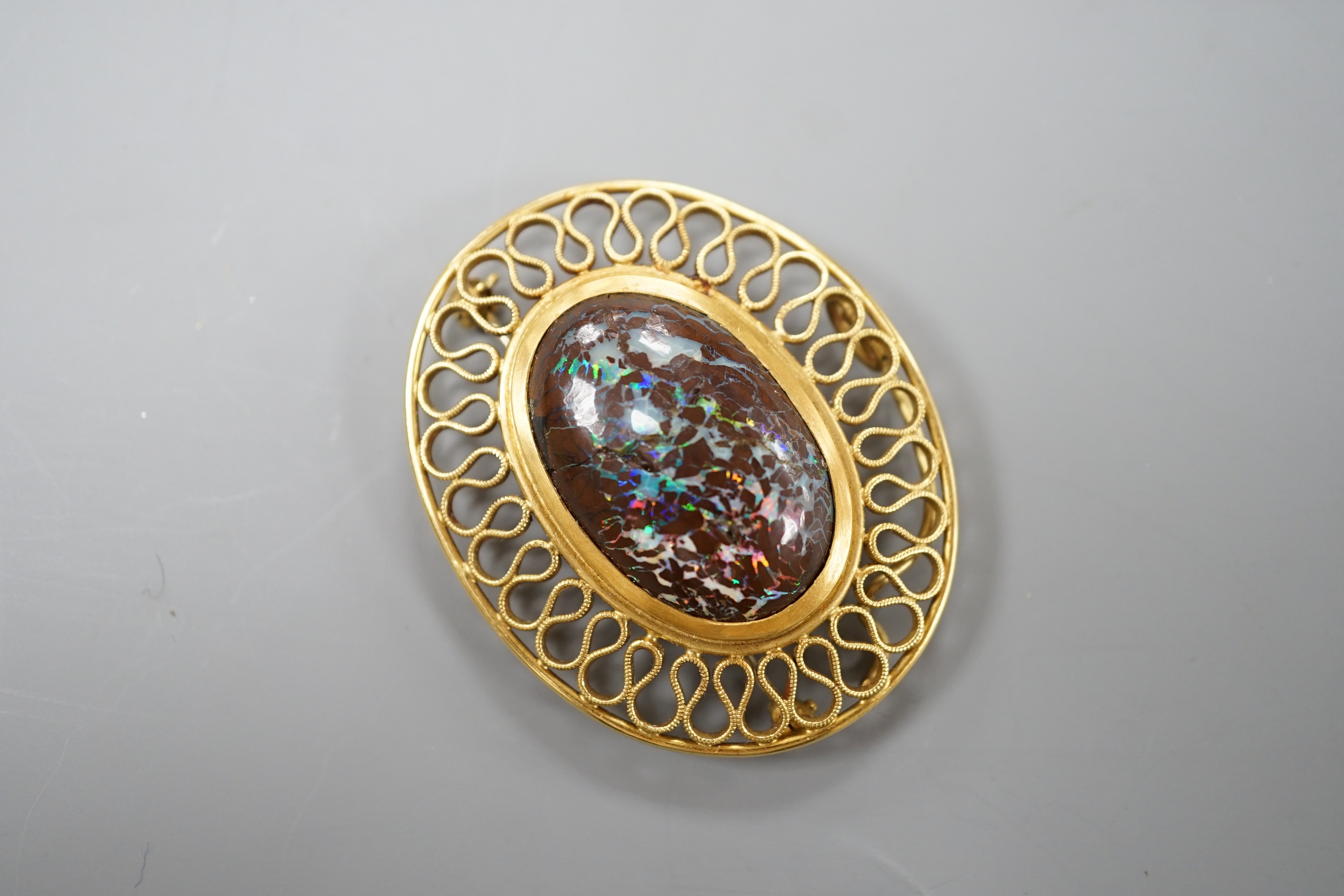 A continental 750 yellow metal and large oval boulder? opal set pendant brooch, with a filigree scroll border, 47mm, gross weight 20 grams (opal cracked).